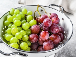 Two varieties of grapes, red and green in a colander. Gray background. Top view.