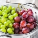 Two varieties of grapes, red and green in a colander. Gray background. Top view.