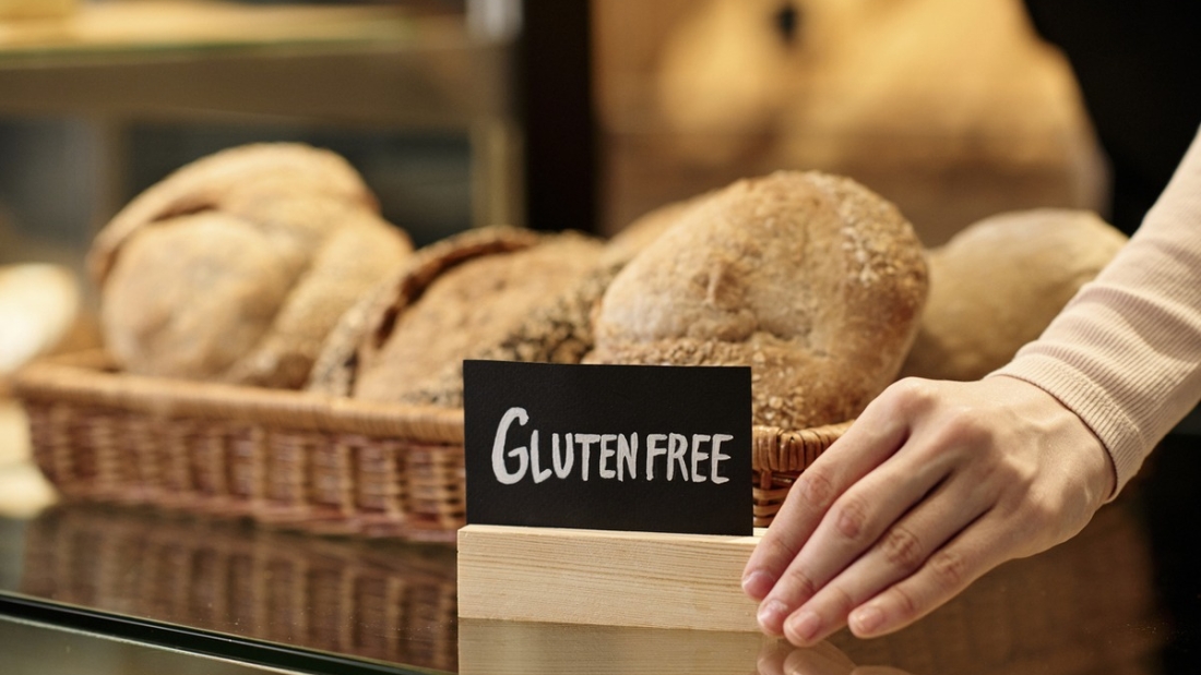 Closeup of fresh breads in artisan bakery with female hand holding gluten free sign, copy space