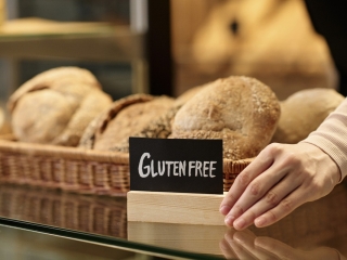 Closeup of fresh breads in artisan bakery with female hand holding gluten free sign, copy space