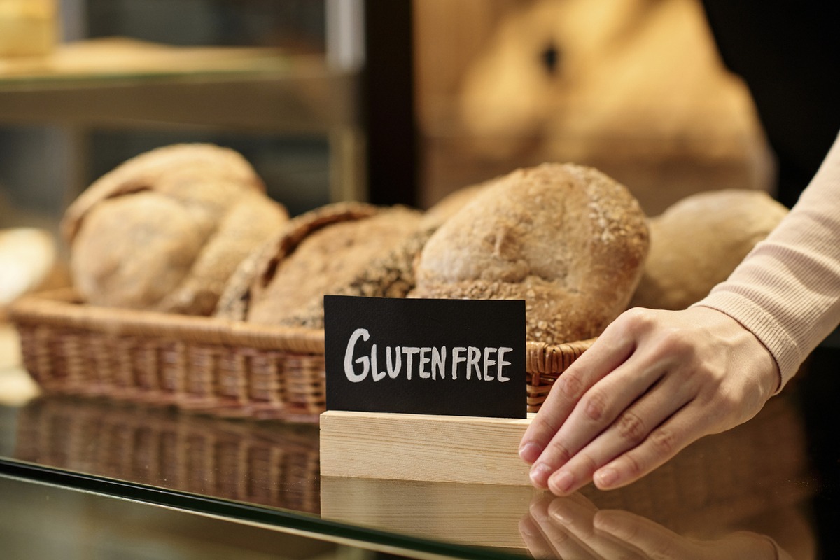 Closeup of fresh breads in artisan bakery with female hand holding gluten free sign, copy space