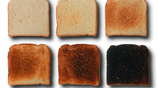 Seis rebanadas de pan con distintos grados de tostado, desde ligeramente doradas hasta quemadas, para representar el aumento de acrilamida durante el calentamiento.